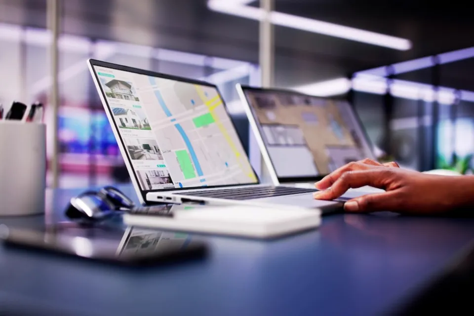 Close-up of hand on laptop keyboard with real estate listings and map pulled up on screen.